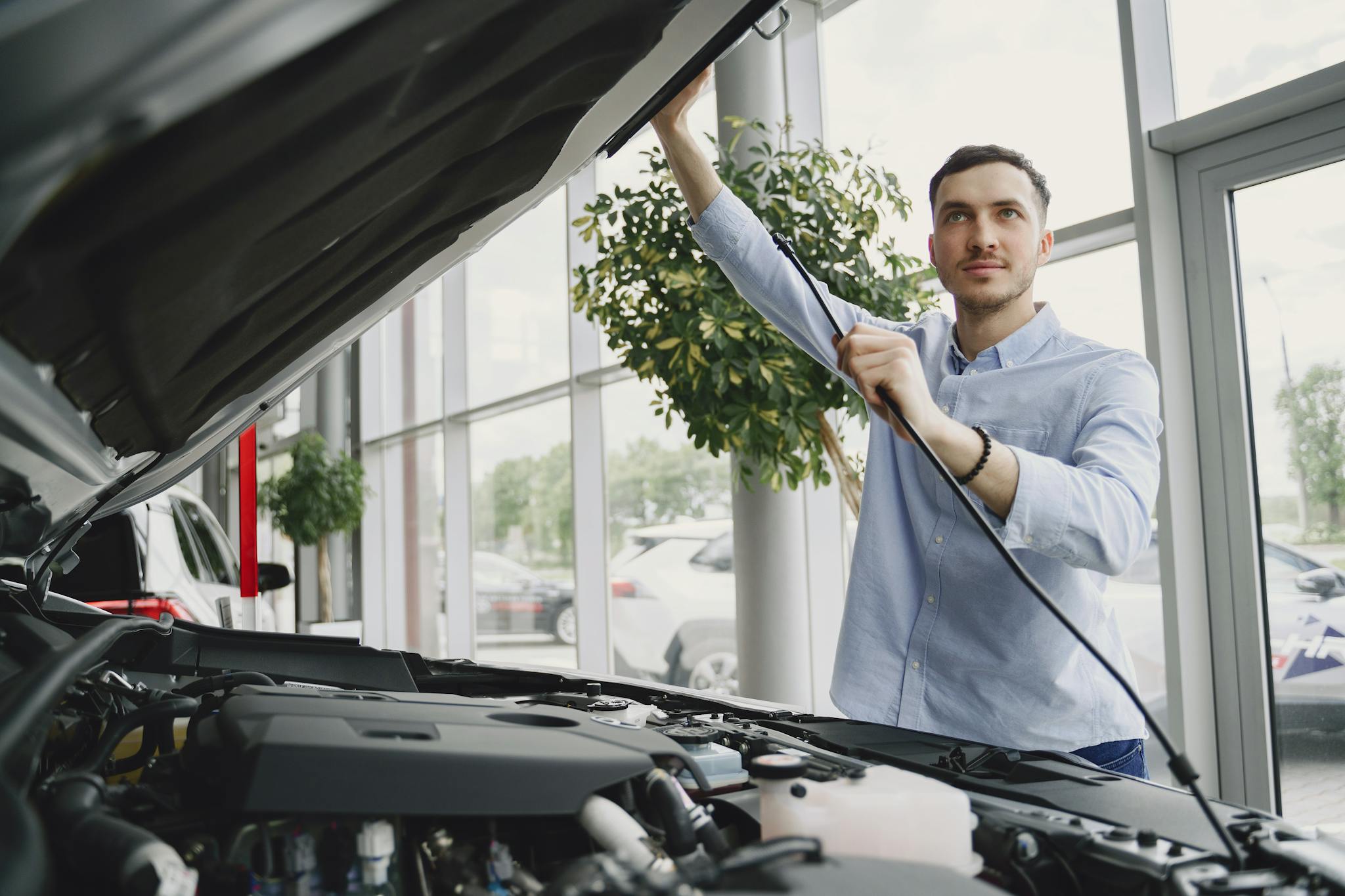 A man carefully checking a car engine in a bright, modern car showroom.