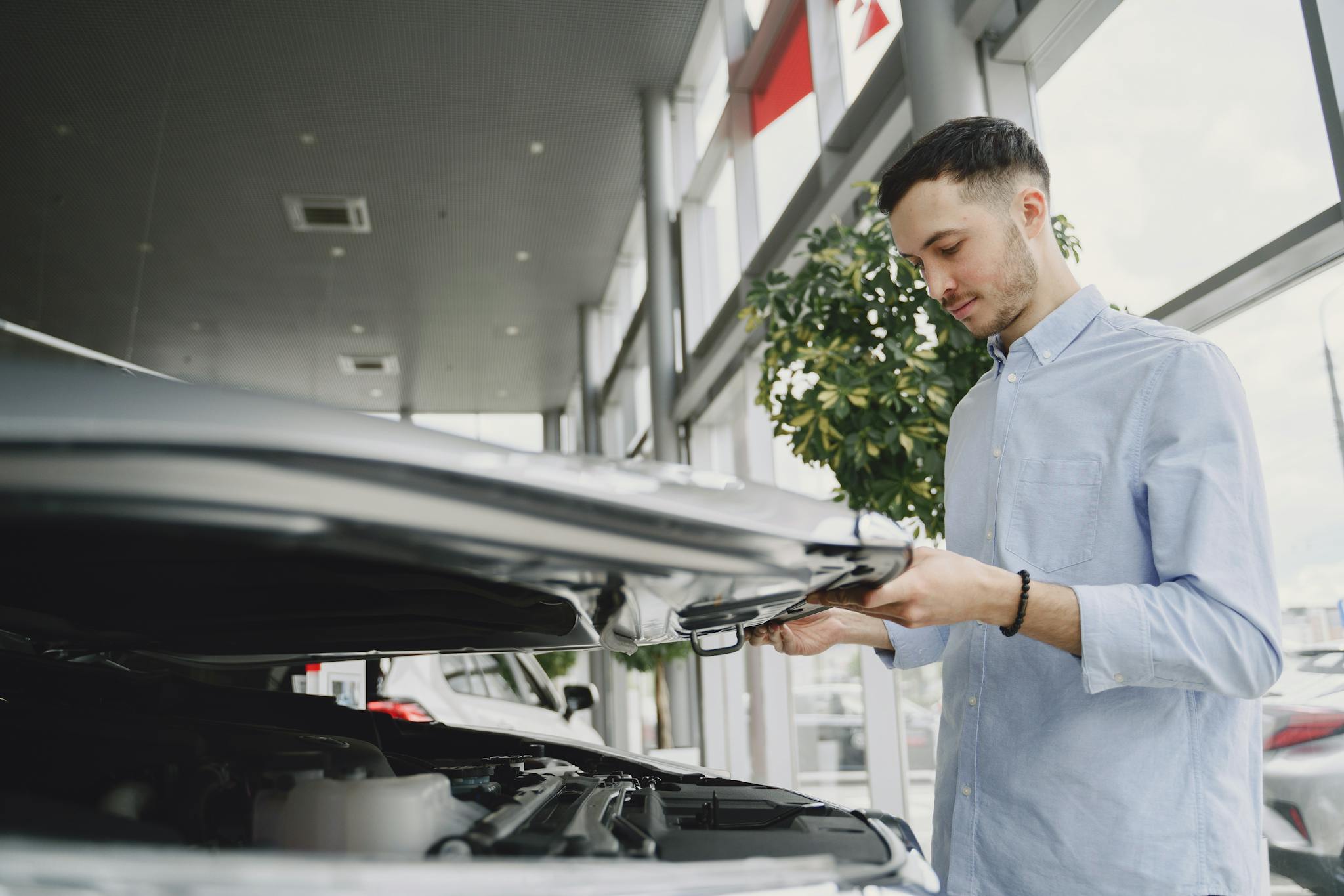 Young man checking car engine in modern dealership showroom.